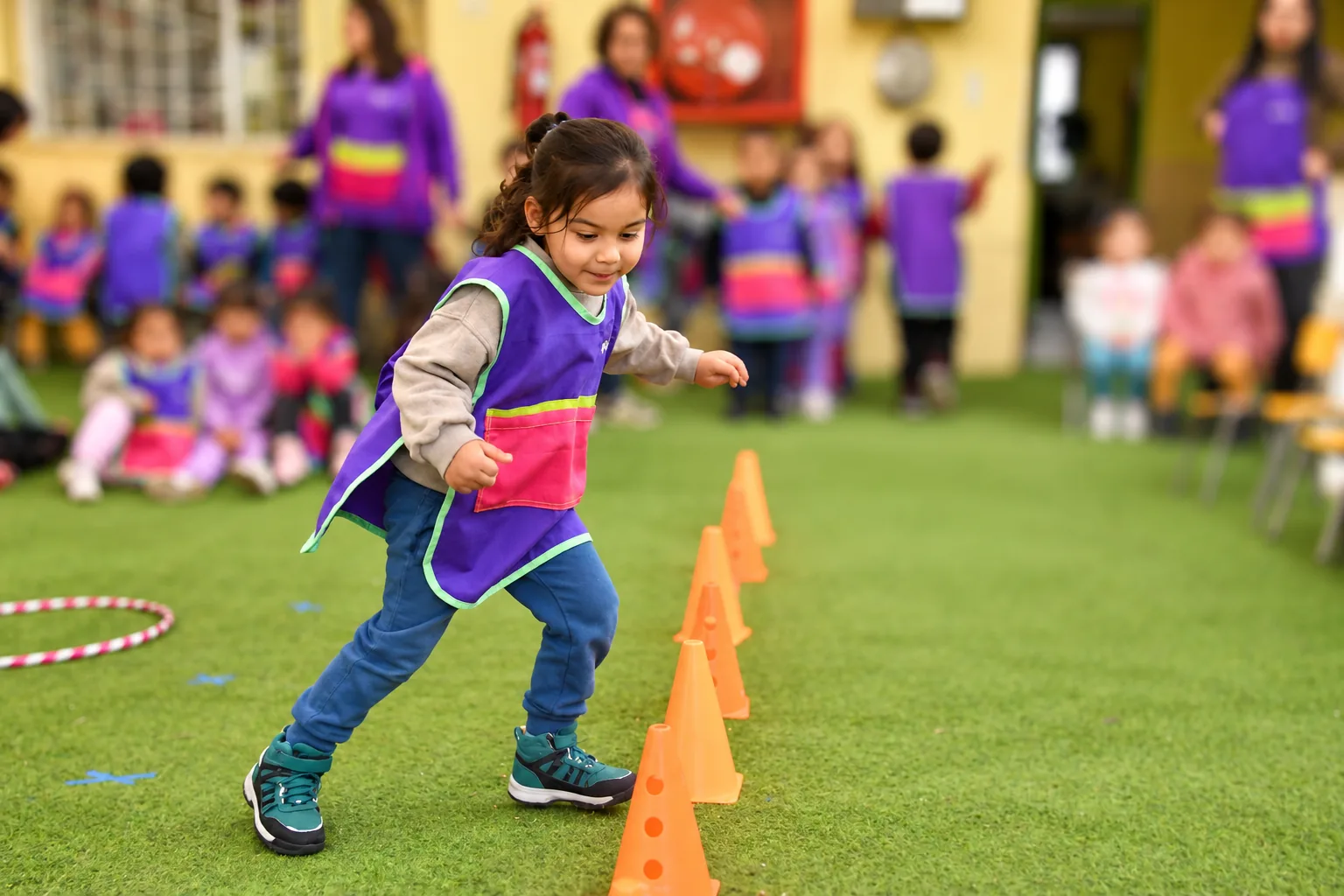Niña realizando un circuito de psicomotricidad con conos en Magos Renca, con participantes desenfocados al fondo